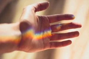 Mano aperta con un arcobaleno di luce che la attraversa, simbolo di inclusione, speranza e diversità.