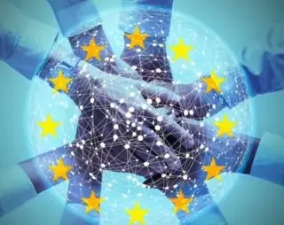 Mani unite che si stringono davanti alla bandiera dell'Unione Europea con le stelle dorate su sfondo blu, simbolo di collaborazione e partnership nell'europrogettazione